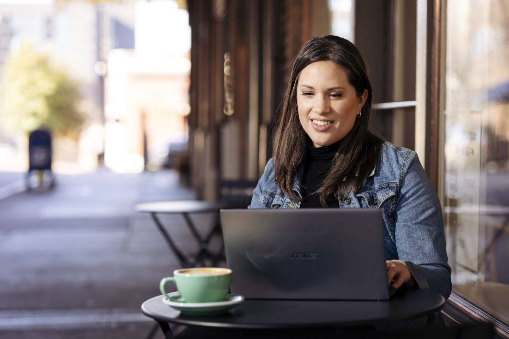 female student sitting outside of a coffee shop working on her laptop