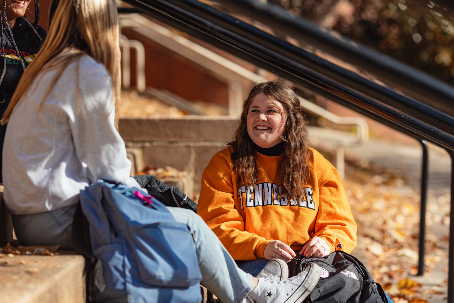 Student Ambassador wearing orange tennessee sweatshirt while sitting on stairs with two other students
