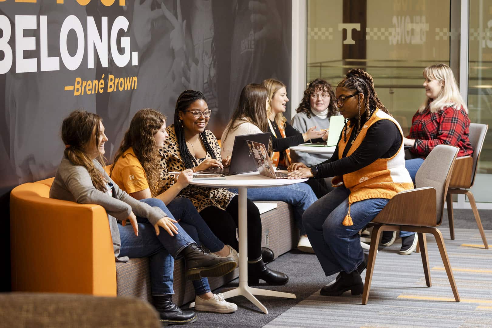 A group of students smiling and working on laptops at a small table