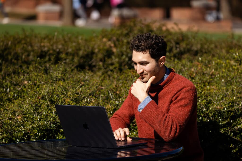 Man looking pensively at his laptop, seated outside