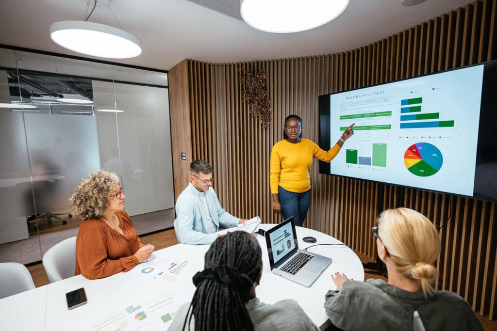 organizational leadership macro social worker leading a meeting in a conference room with a presentation on a screen behind her