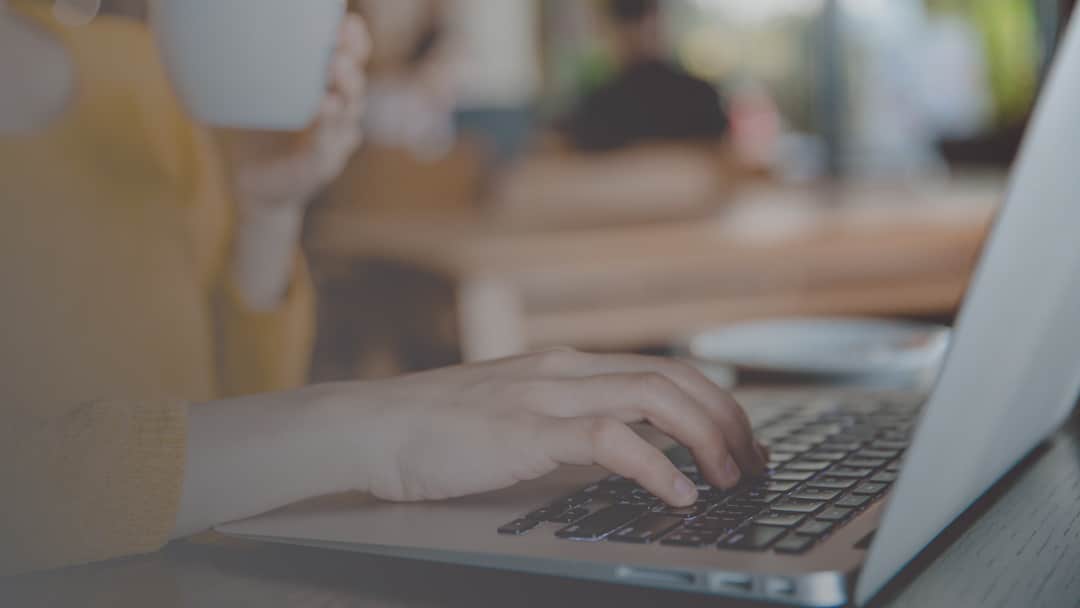 woman's hands typing on laptop and drinking coffee