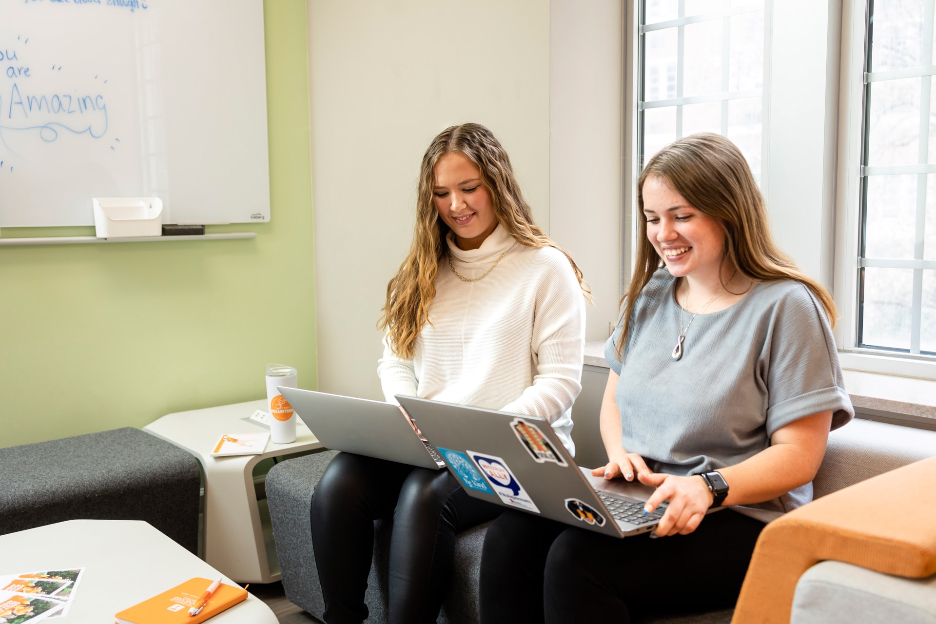 Two students sitting on a couch, working on laptops