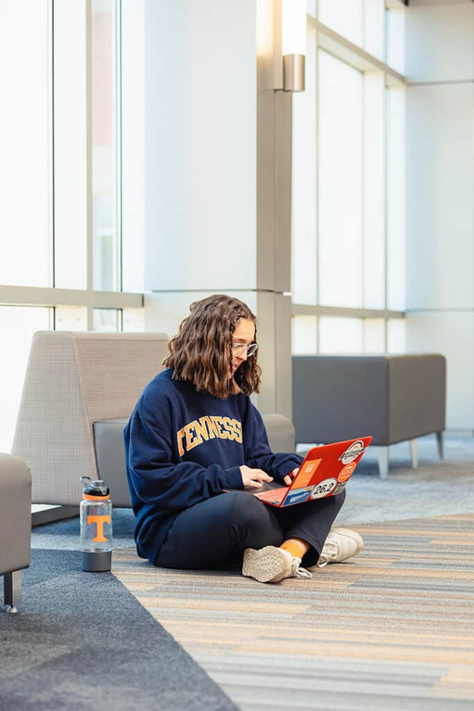 Cecily strong working on laptop while sitting on the floor in the Student Union