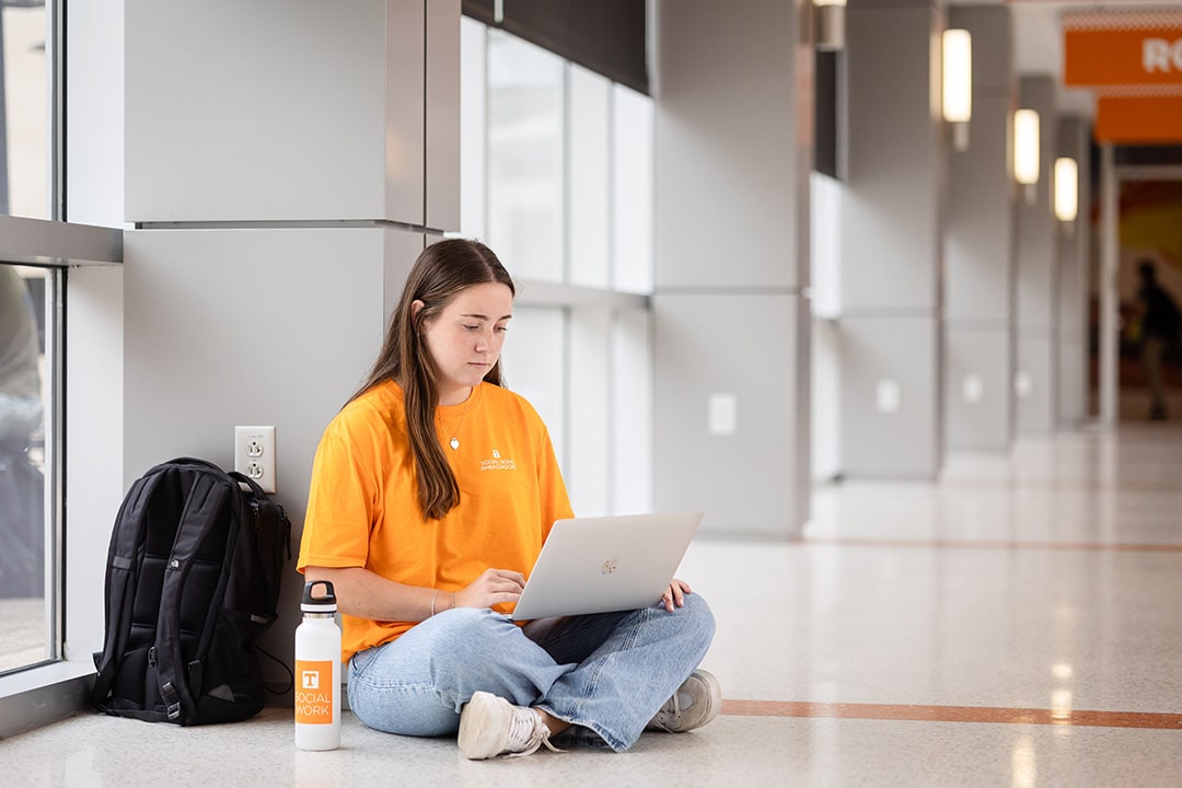 social work student sitting on floor working on a laptop