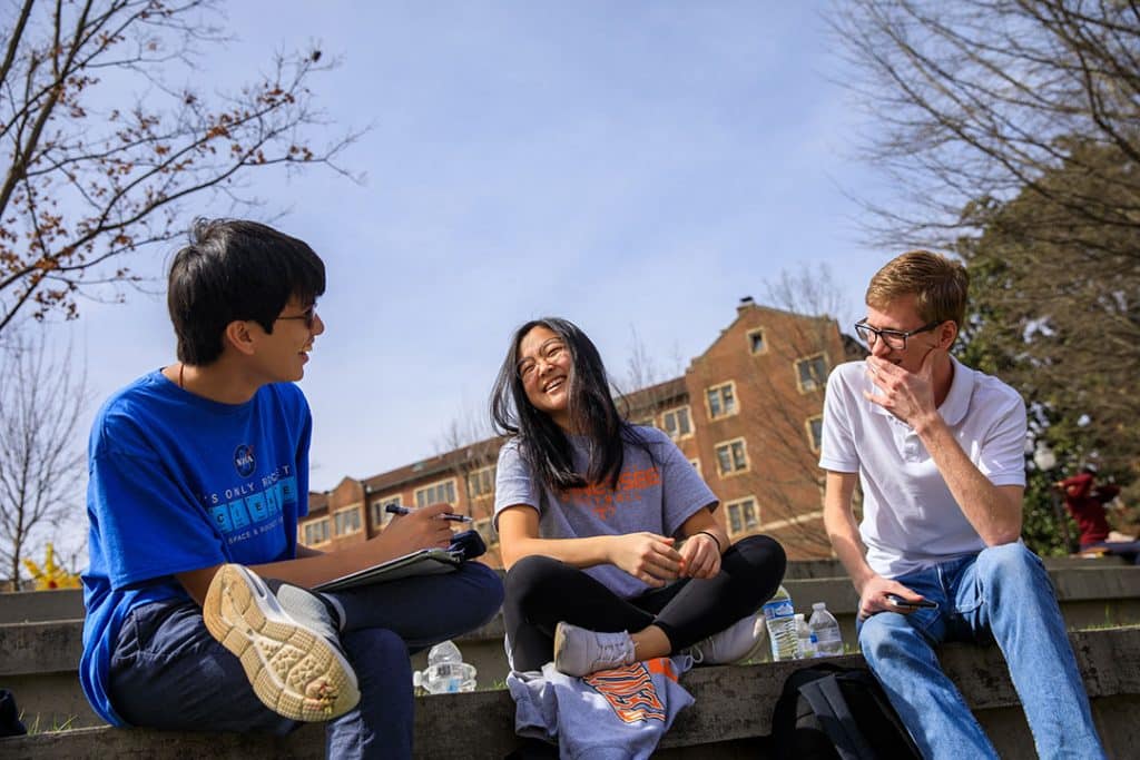 Three students gathered in a courtyard, laughing