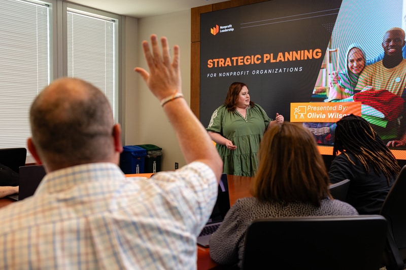man in business meeting raising hand while presenter speaks