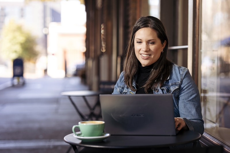 woman sits outside of coffee shop while doing grad school class on her laptop