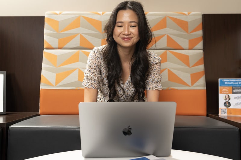 online mssw student working on laptop while sitting on a orange patterned couch