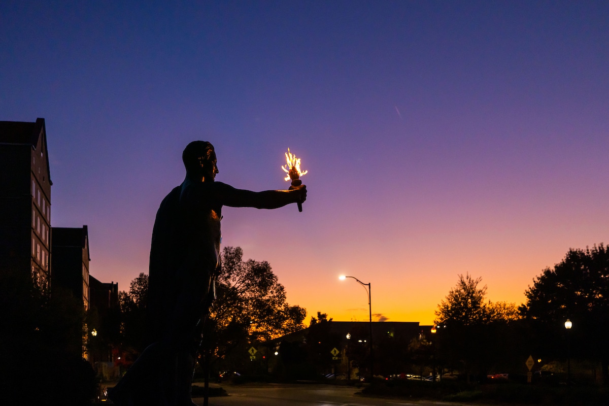Silhouettes of the Torchbearer Statue in Circle Park as the sun sets across campus