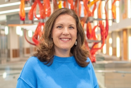 Sarah Arnold in a blue sweatshirt with a blurred background featuring a red and orange abstract art installation.
