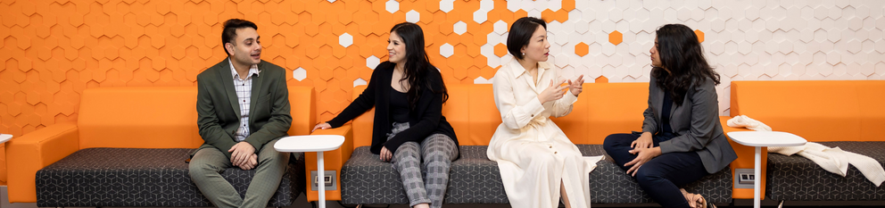 PhD students sitting on couch in front of orange and white wall