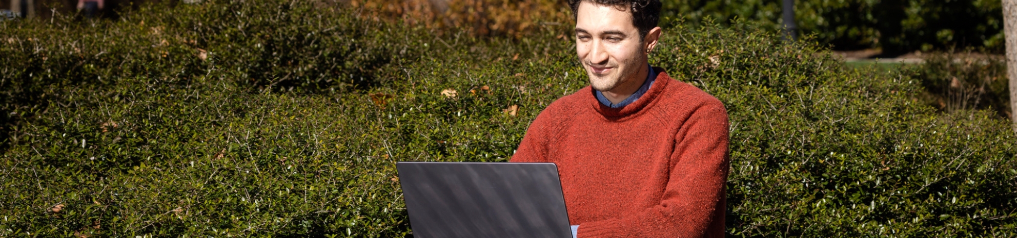 student in red sweater working on laptop outside