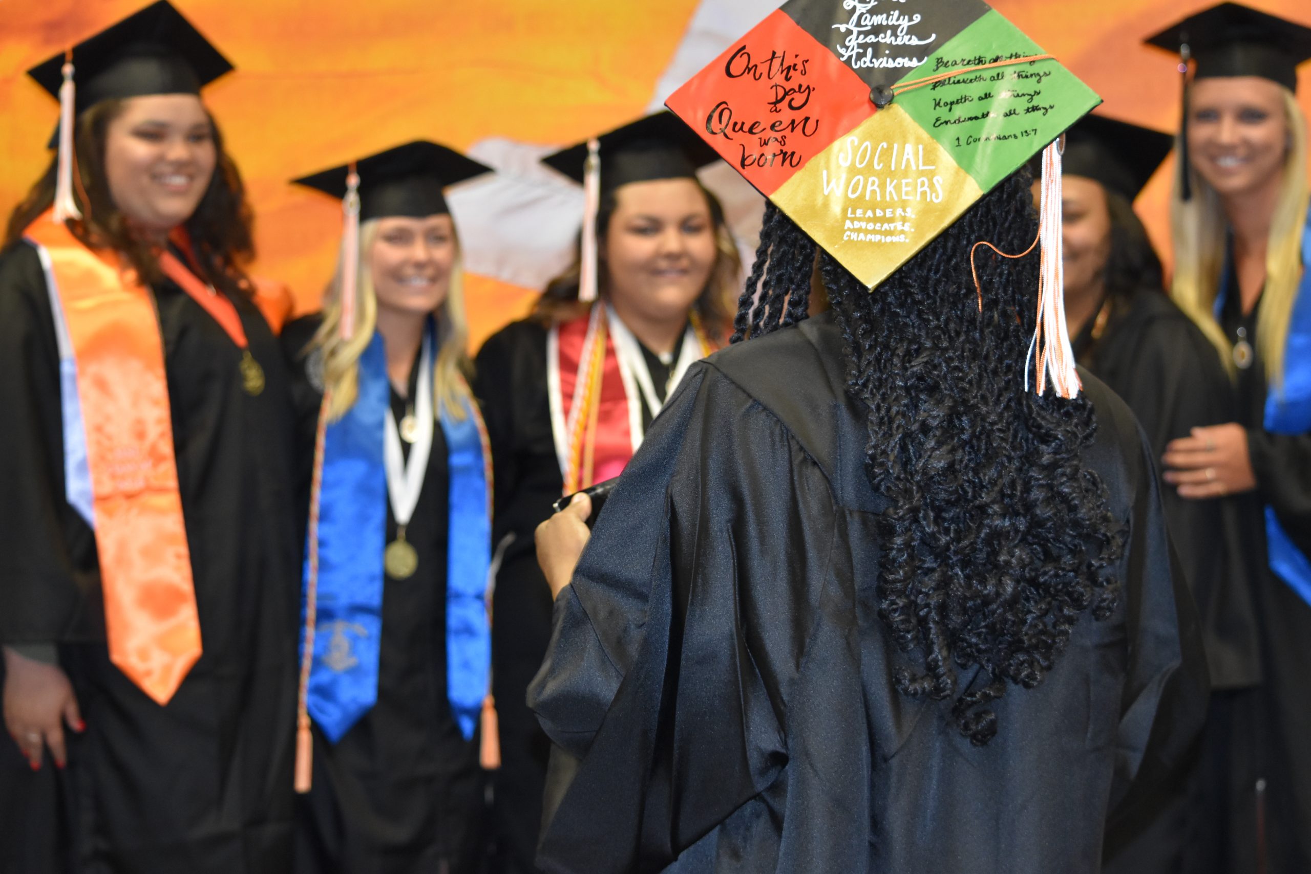 college graduates wearing caps and gowns standing in front of an orange wall