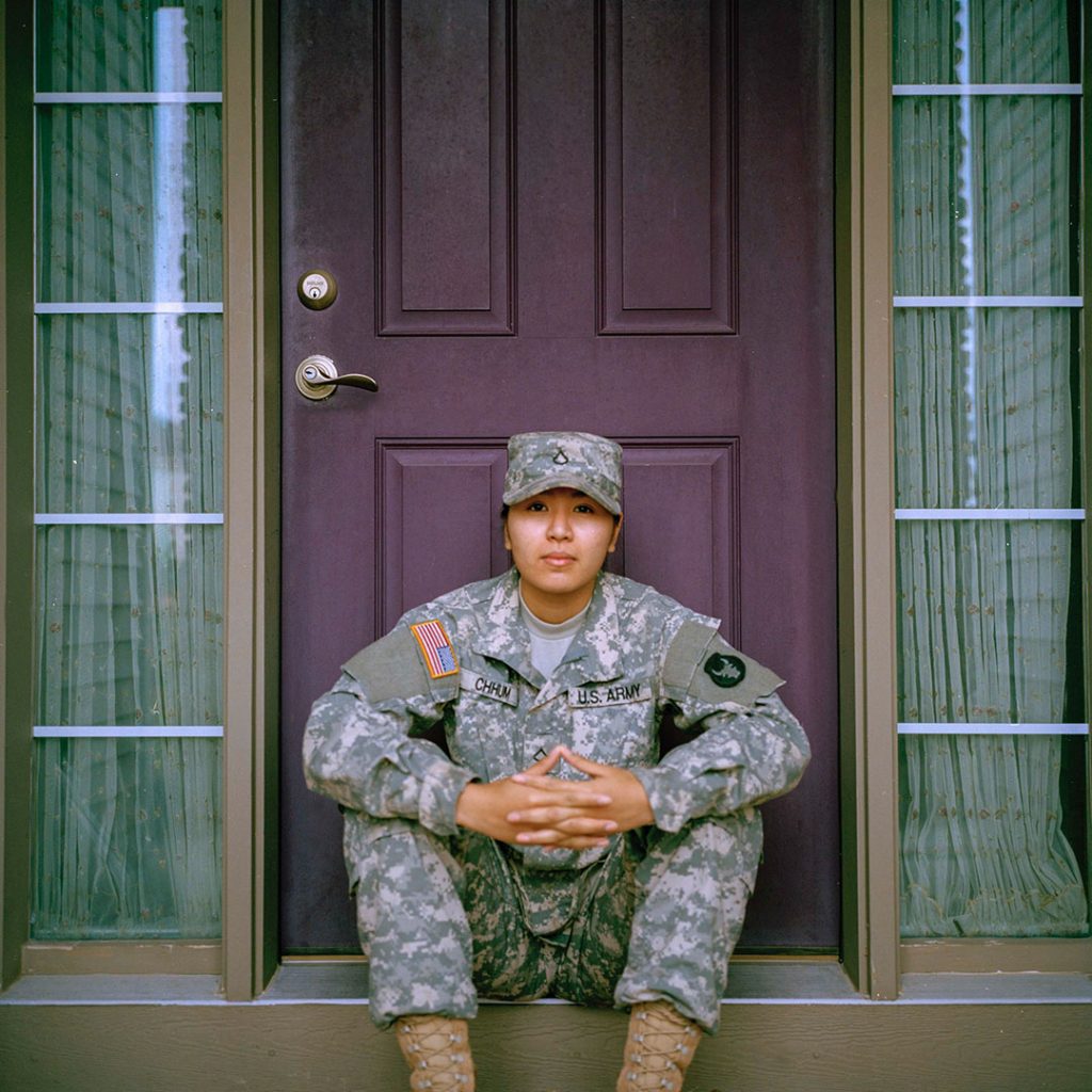 female in army uniform sitting on stoop looking into camera